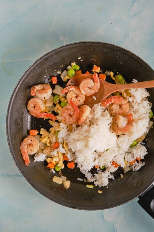 Shrimp stir-fry with rice, vegetables, and scrambled eggs in a black skillet.