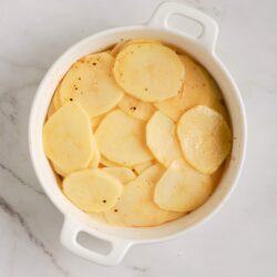 Thinly sliced potatoes in a white baking dish ready for baking or roasting.