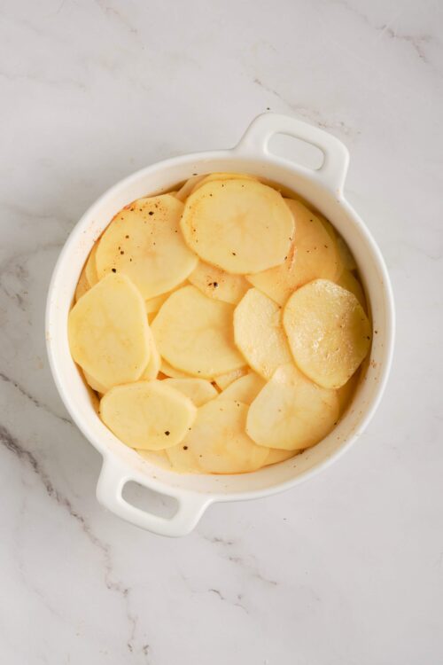 Thinly sliced potatoes in a white baking dish ready for baking or roasting.