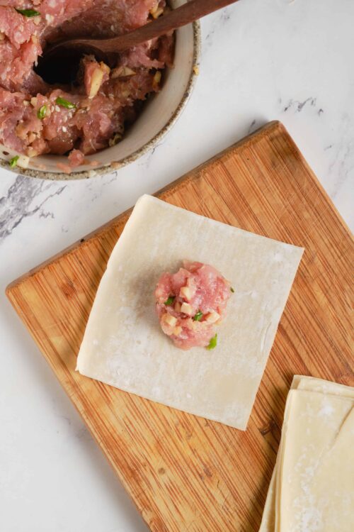 Seasoned ground chicken and vegetable mixture for dumplings on wooden cutting board.