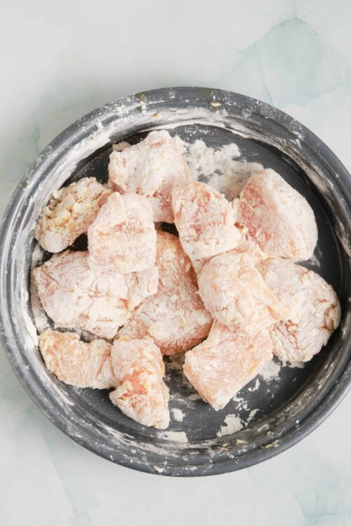 Flour-coated chicken pieces in a mixing bowl, ready for cooking or breading.
