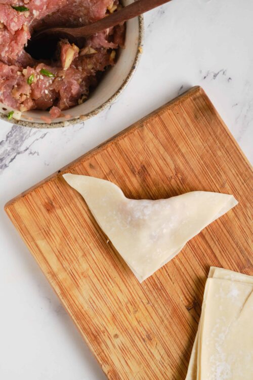 Fresh homemade cheese tortellini on a wooden cutting board with ground meat filling in the background.