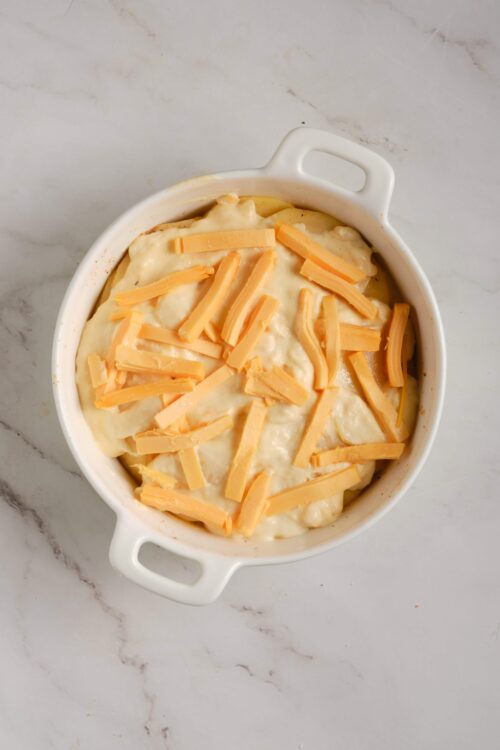 Creamy cheesy baked potato casserole topped with shredded cheddar cheese, ready to bake.