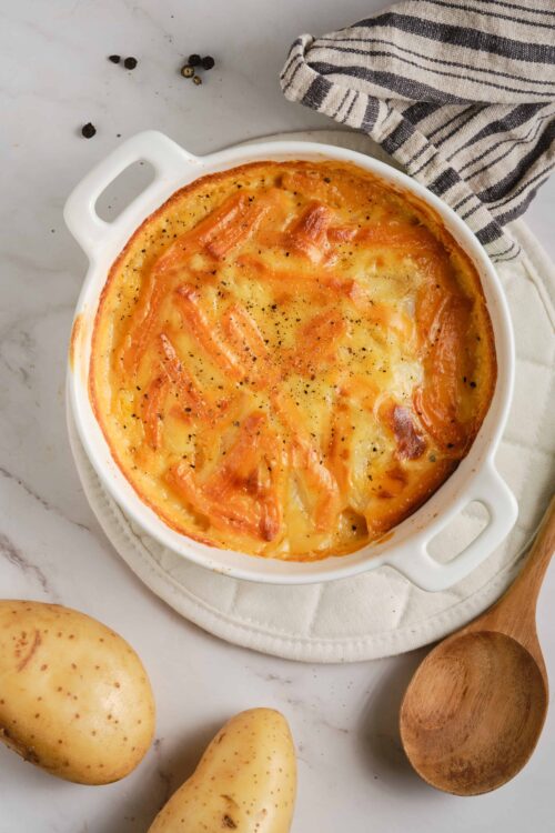 Creamy baked salmon potato casserole with melted cheese, fresh salmon, and black pepper in a white dish.