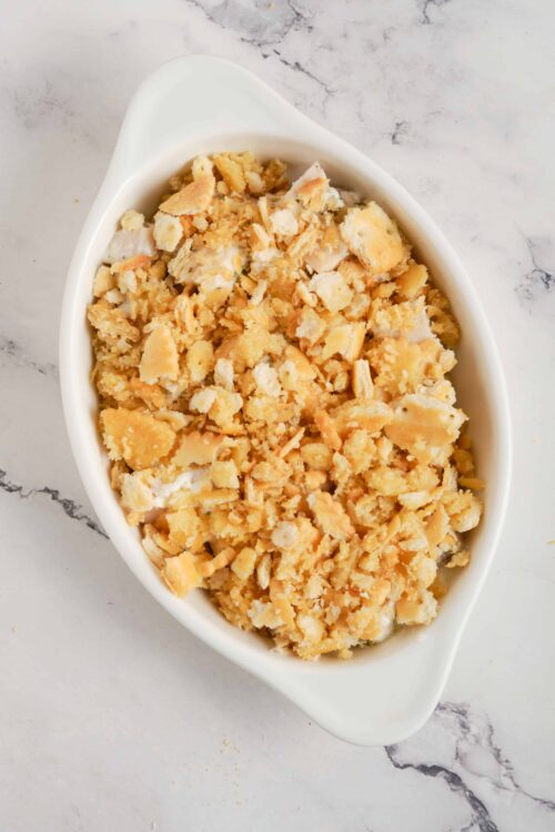 Shredded chicken and cheese casserole topping with crumbled crackers in a white baking dish.
