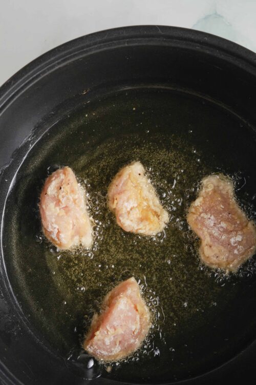 Crispy breaded chicken nuggets frying in a skillet.