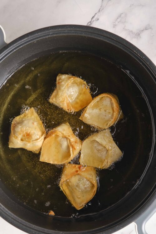 Fried wontons cooking in a skillet with hot oil.