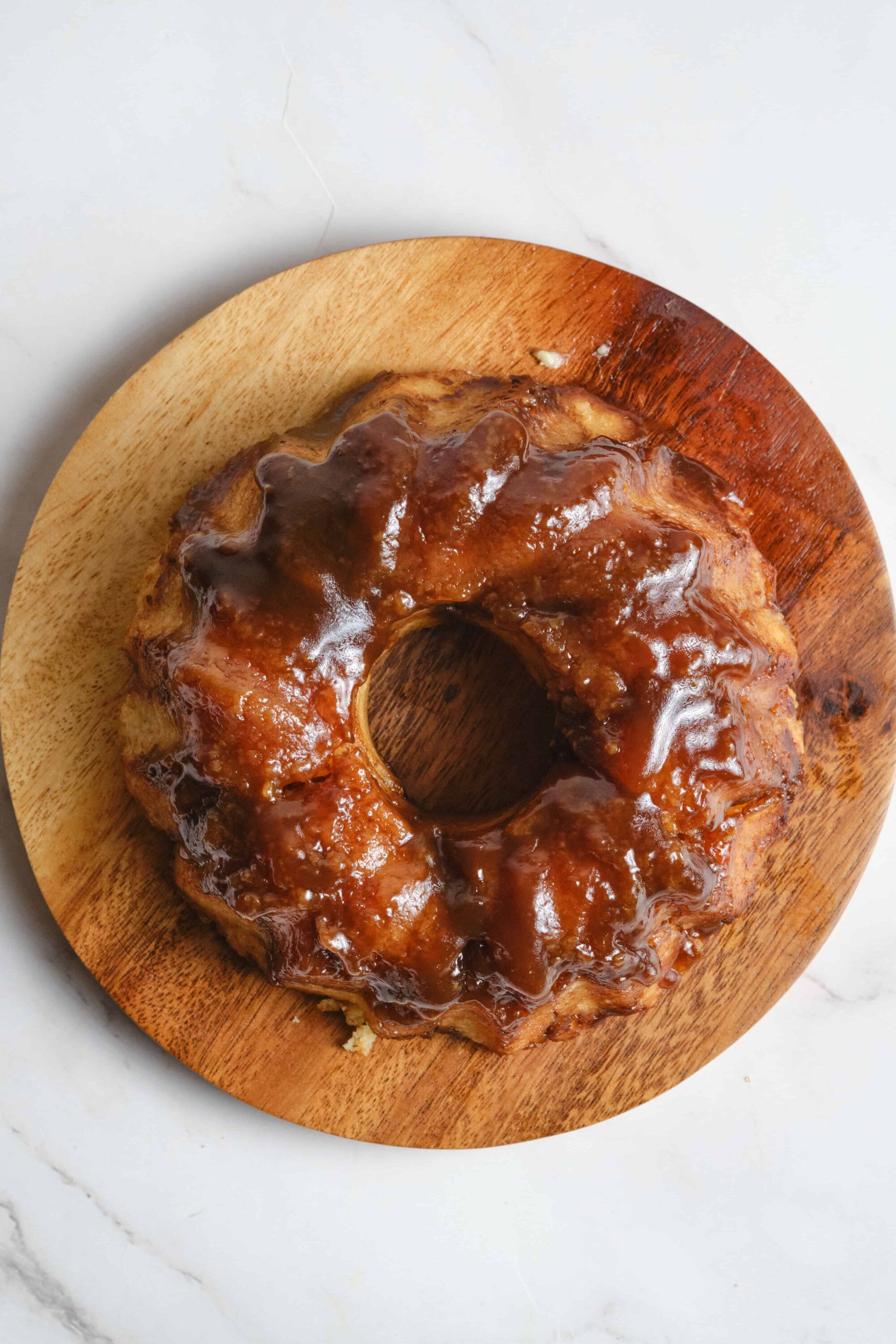 Buttery caramel cinnamon roll cake drizzled with caramel glaze on wooden board.