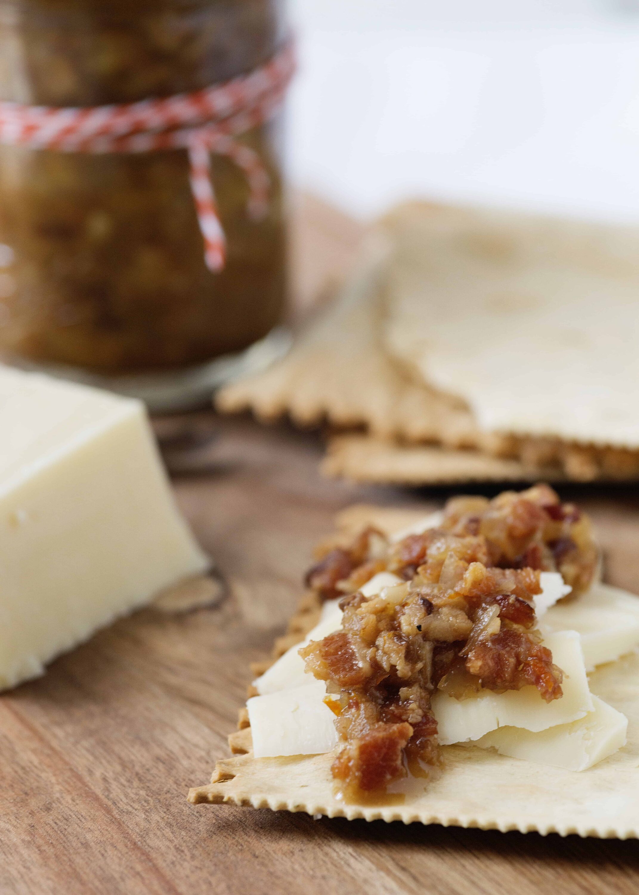 Savory cheese and bacon spread on a cracker with a jar of chutney in the background.