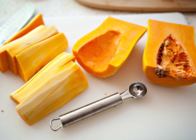 Sweet and savory butternut squash and pumpkin squash on a white cutting board with a melon baller utensil.
