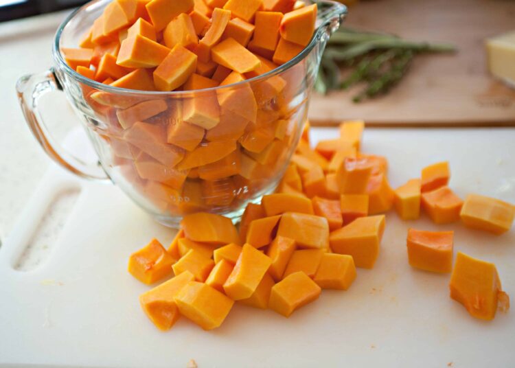 Diced butternut squash in a glass measuring cup on a white cutting board.