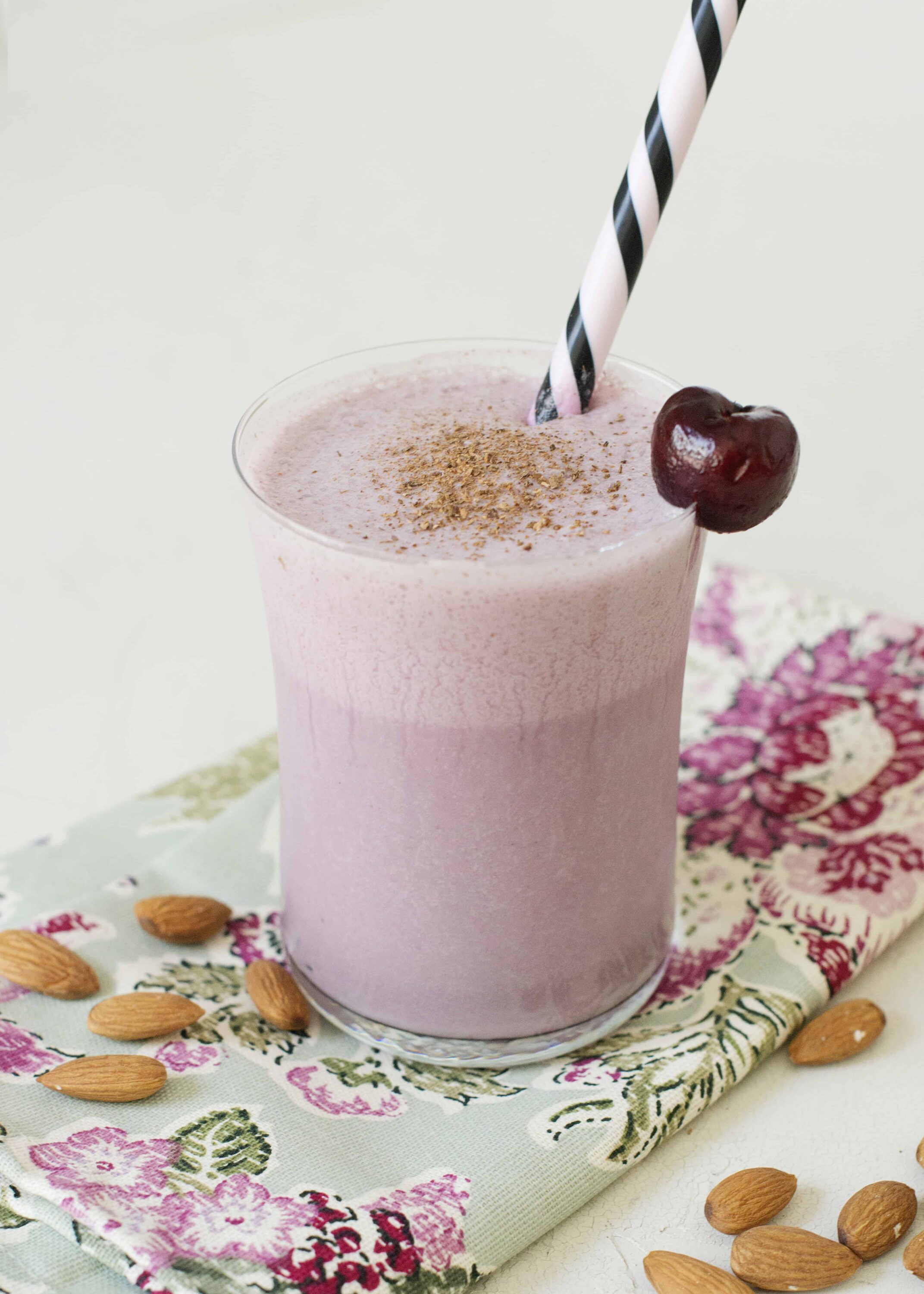 Creamy cherry almond smoothie in a glass with a striped straw, garnished with a cherry.