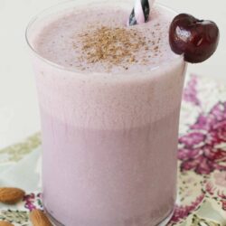 Creamy cherry smoothie with chocolate garnish and striped straw in a tall glass.