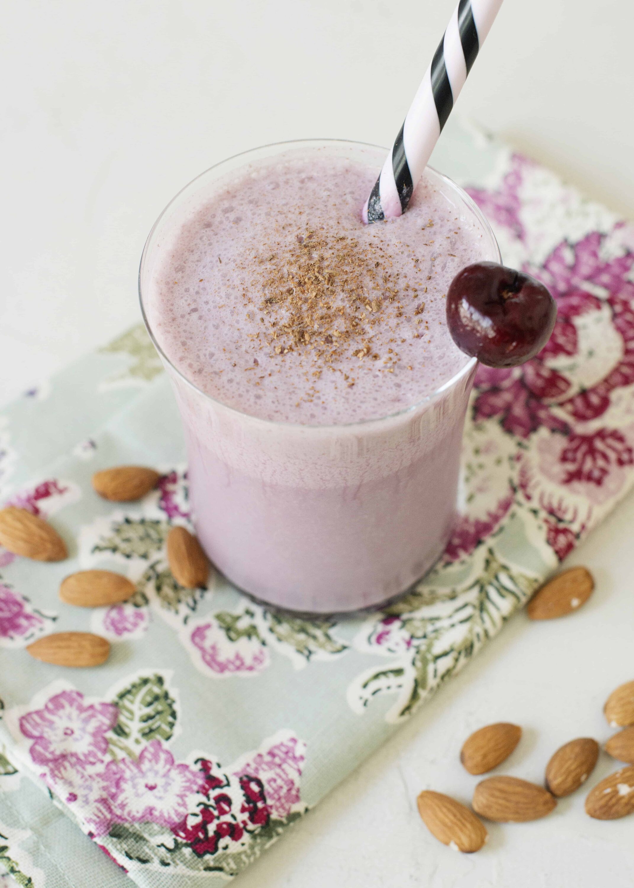 Creamy cherry almond smoothie with cherry garnish, served in a clear glass with a striped straw.