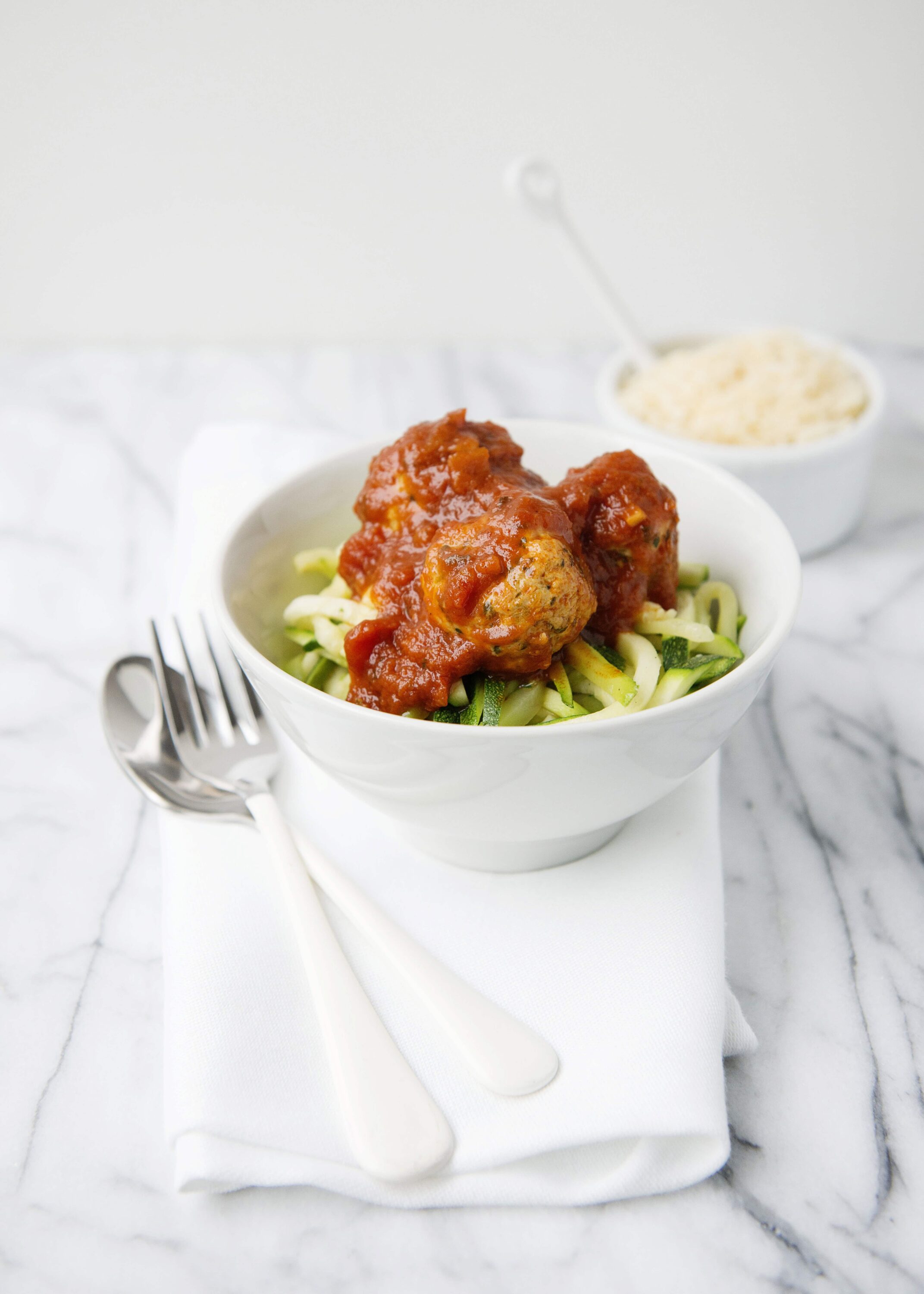 Savory meatball and zucchini noodles with marinara sauce in a white bowl.