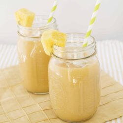 Creamy pineapple smoothie served in mason jars with striped straws and pineapple garnish. Refreshing summer beverage perfect for breakfast or snack.