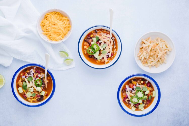 Cheesy chili in Bowls with fresh toppings and shredded cheese on side.