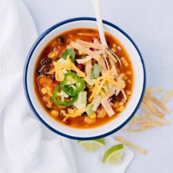 Fresh bowl of Mexican soup with beans, corn, and shredded cheese garnished with jalapenos, cilantro, and tortilla strips.