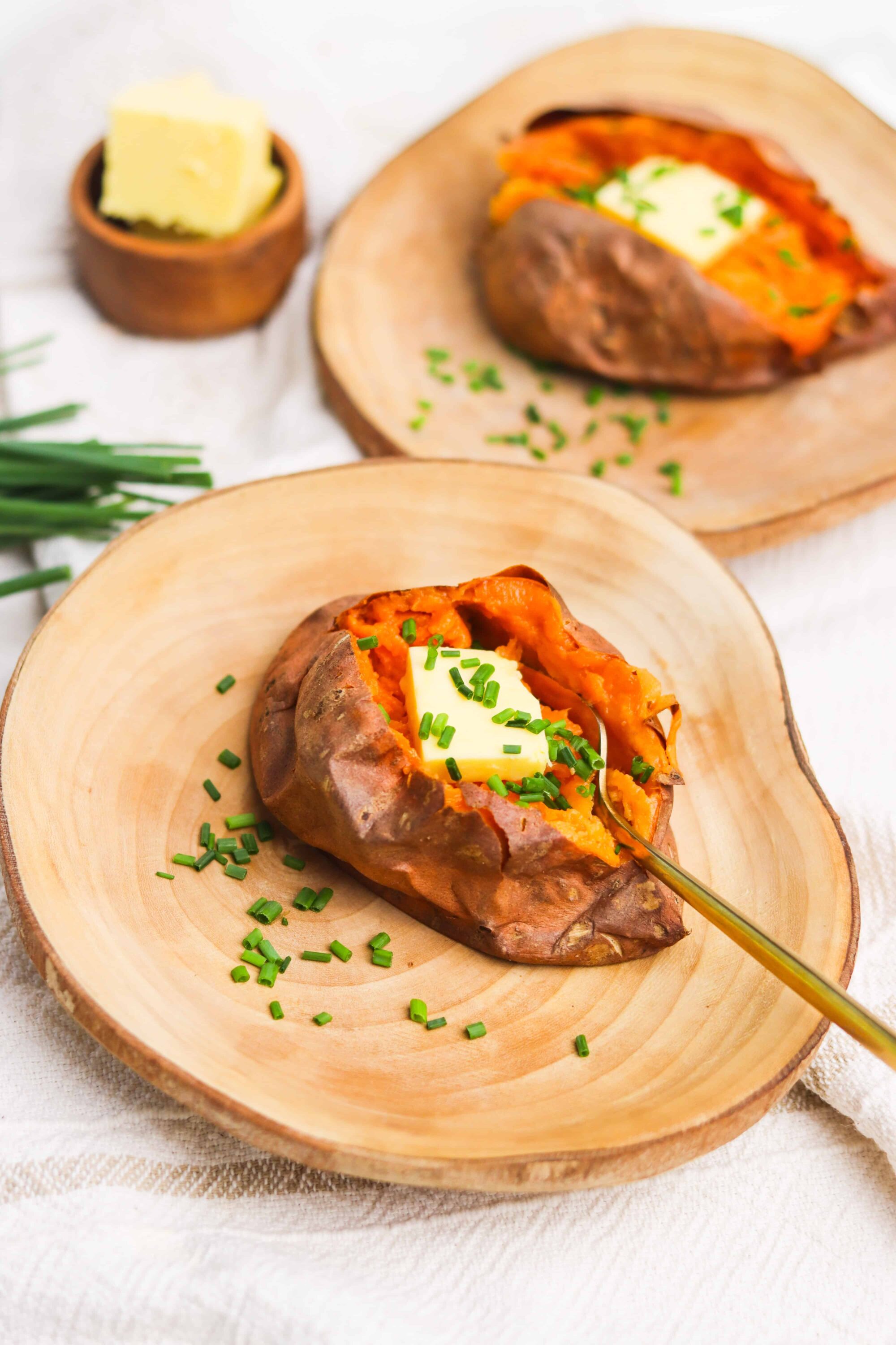 Baked sweet potato with butter and chives on a wooden plate, delicious healthy side dish.