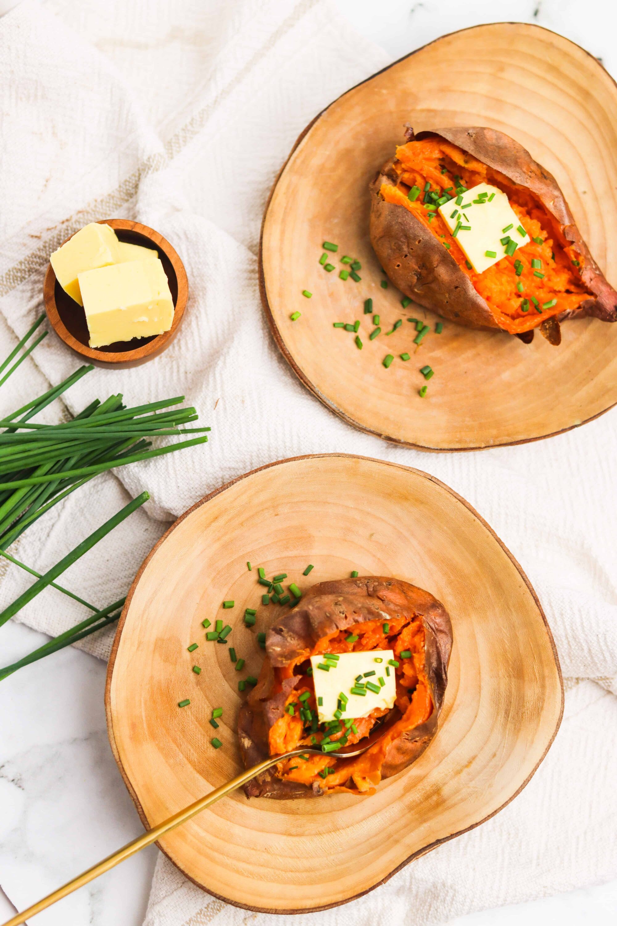 Golden baked sweet potato stuffed with butter and chives on rustic wooden plates.