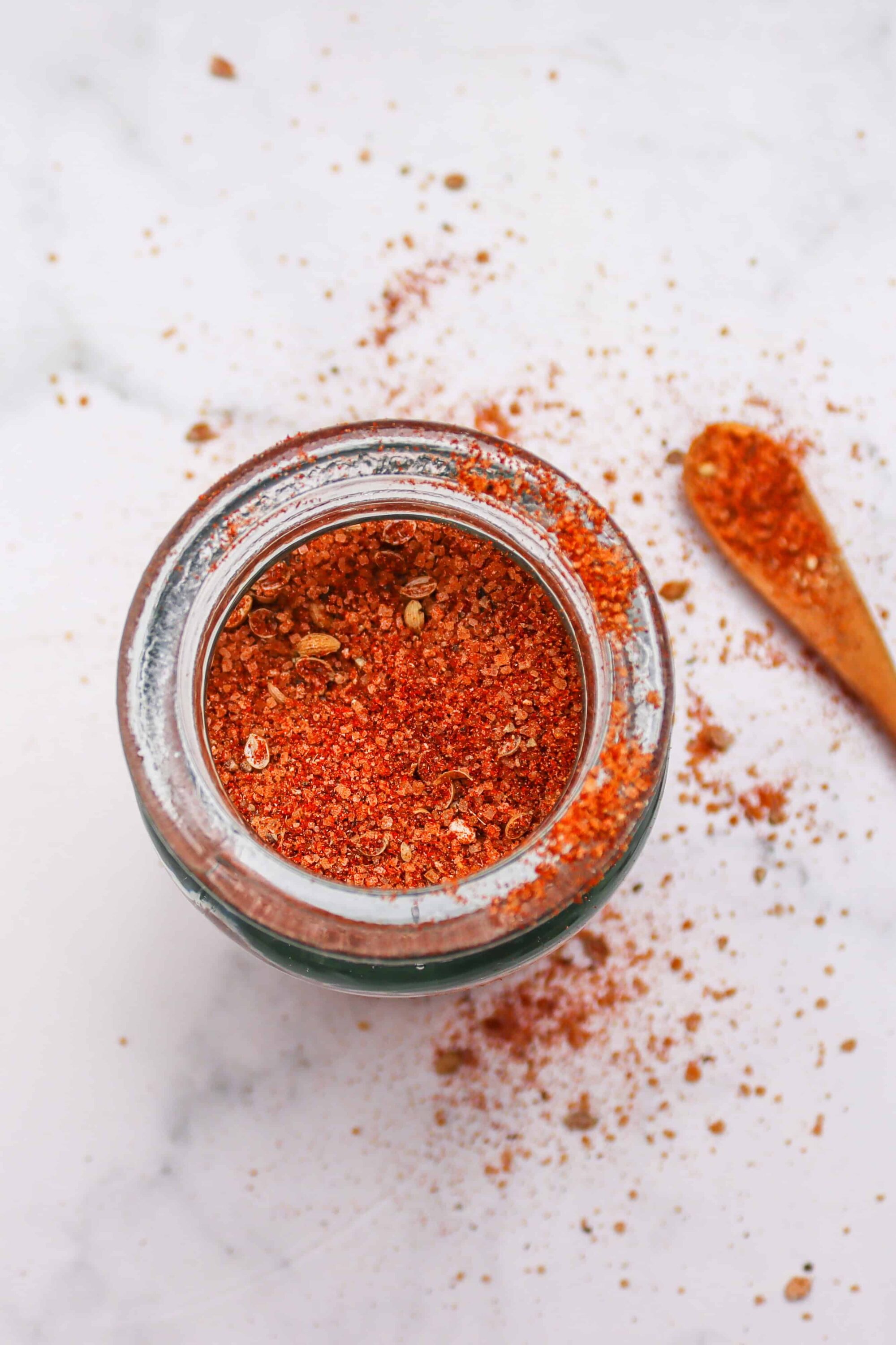 Ground paprika spice in a glass jar with a wooden spoon on a white surface.