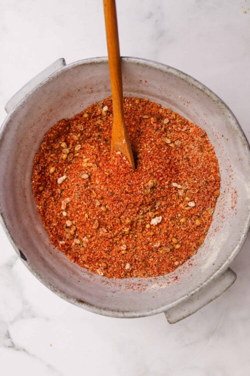 Coarse chili spice blend in a metal bowl with a wooden spoon, ready for cooking.
