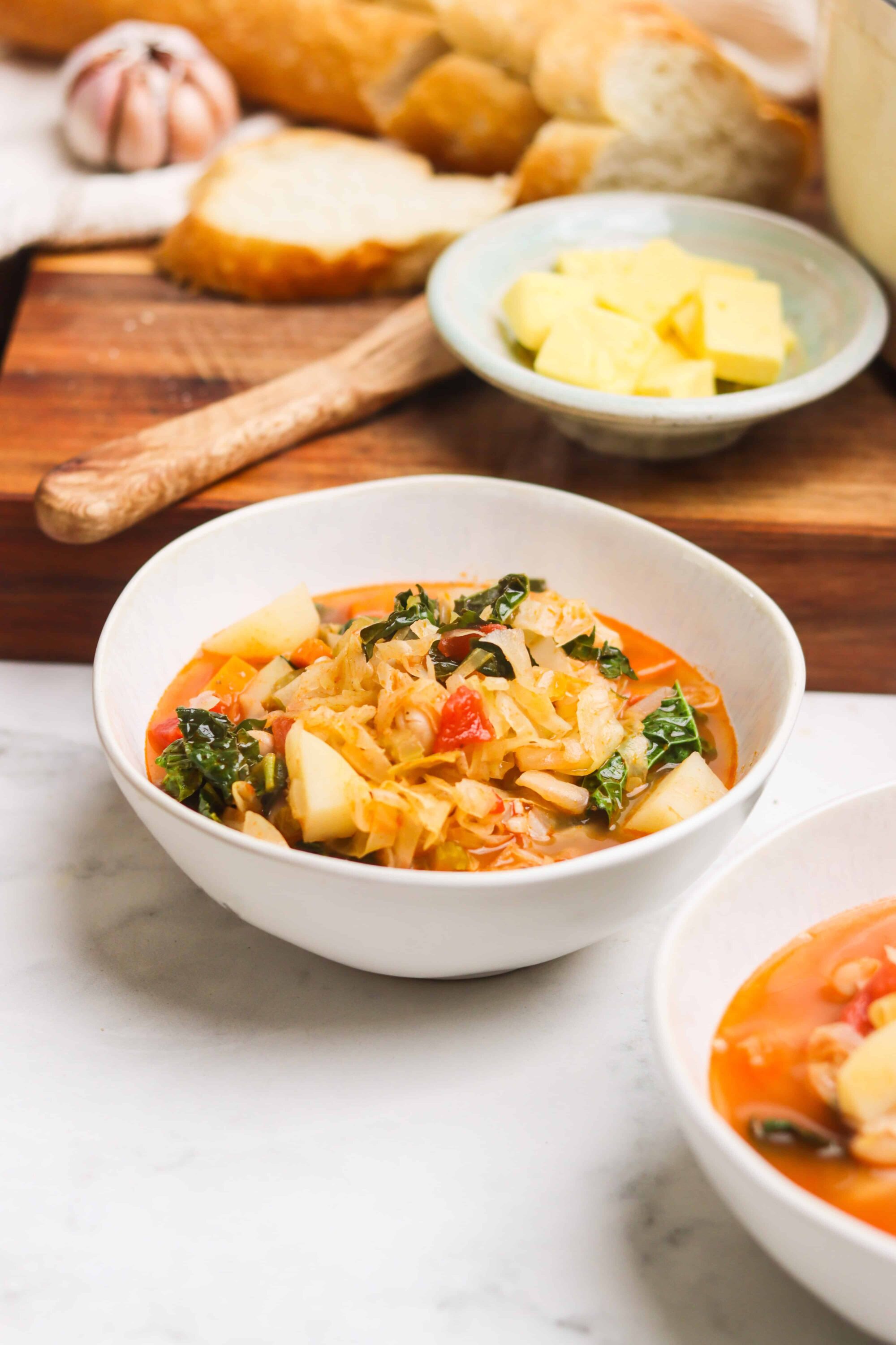 Creamy vegan sauerkraut soup with fresh vegetables in a white bowl.