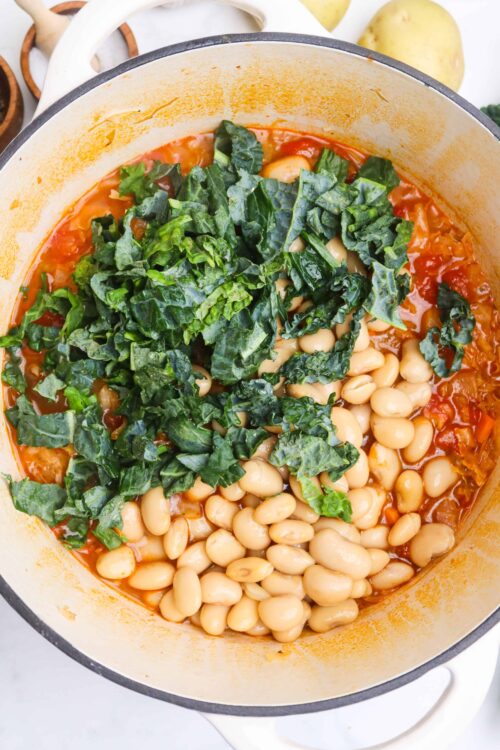 Creamy white beans and kale stew in a white pot.