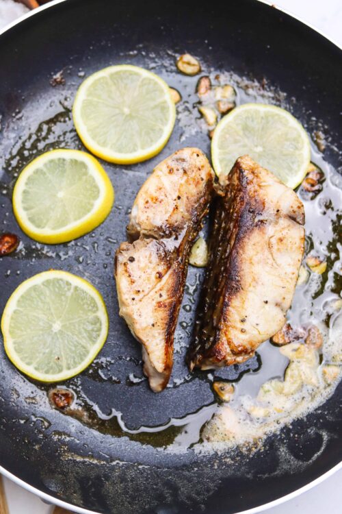 Juicy pan-seared chicken breasts with lemon slices and garlic in a black skillet.