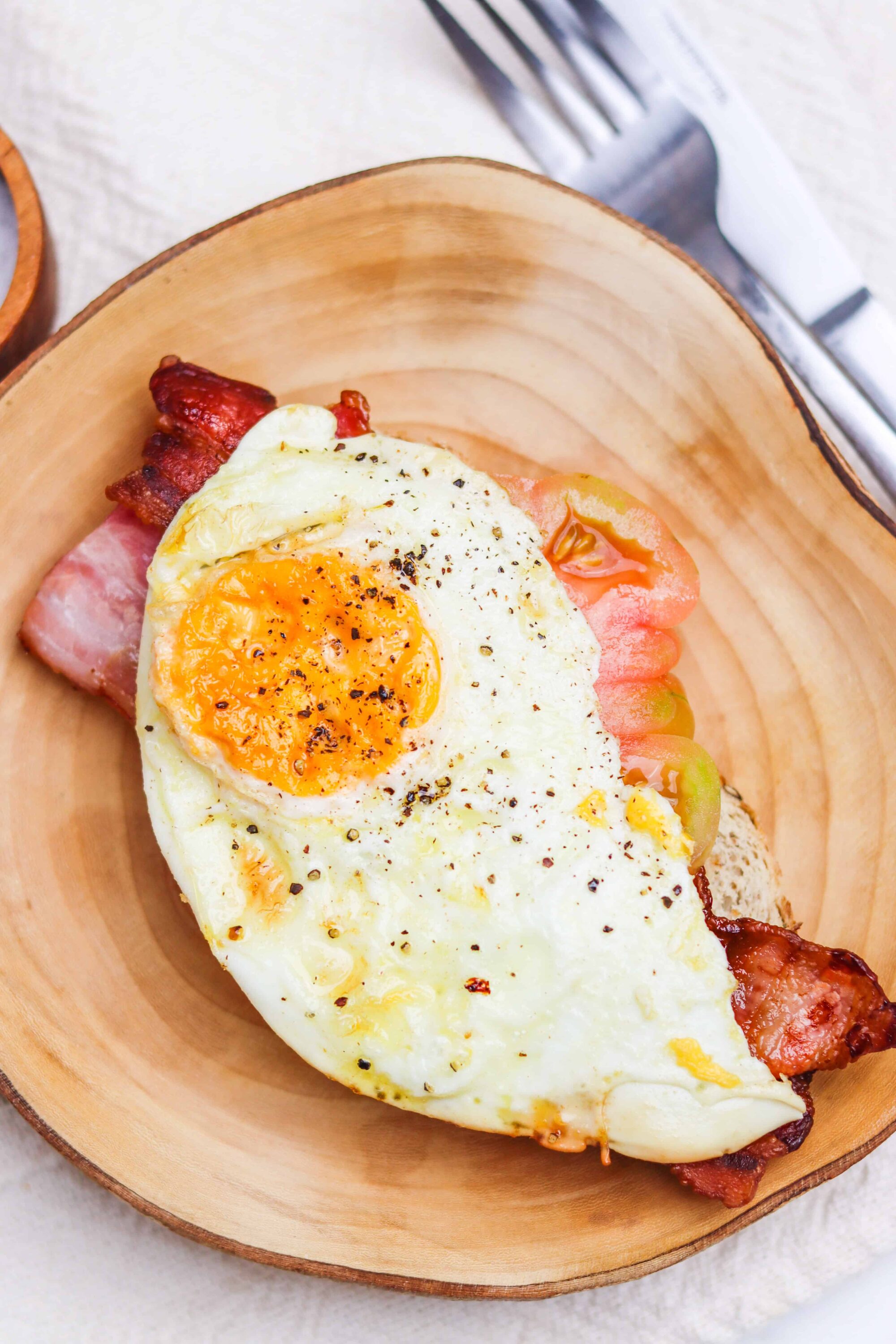 Savory breakfast baked egg in bacon and ham meal in wooden bowl.