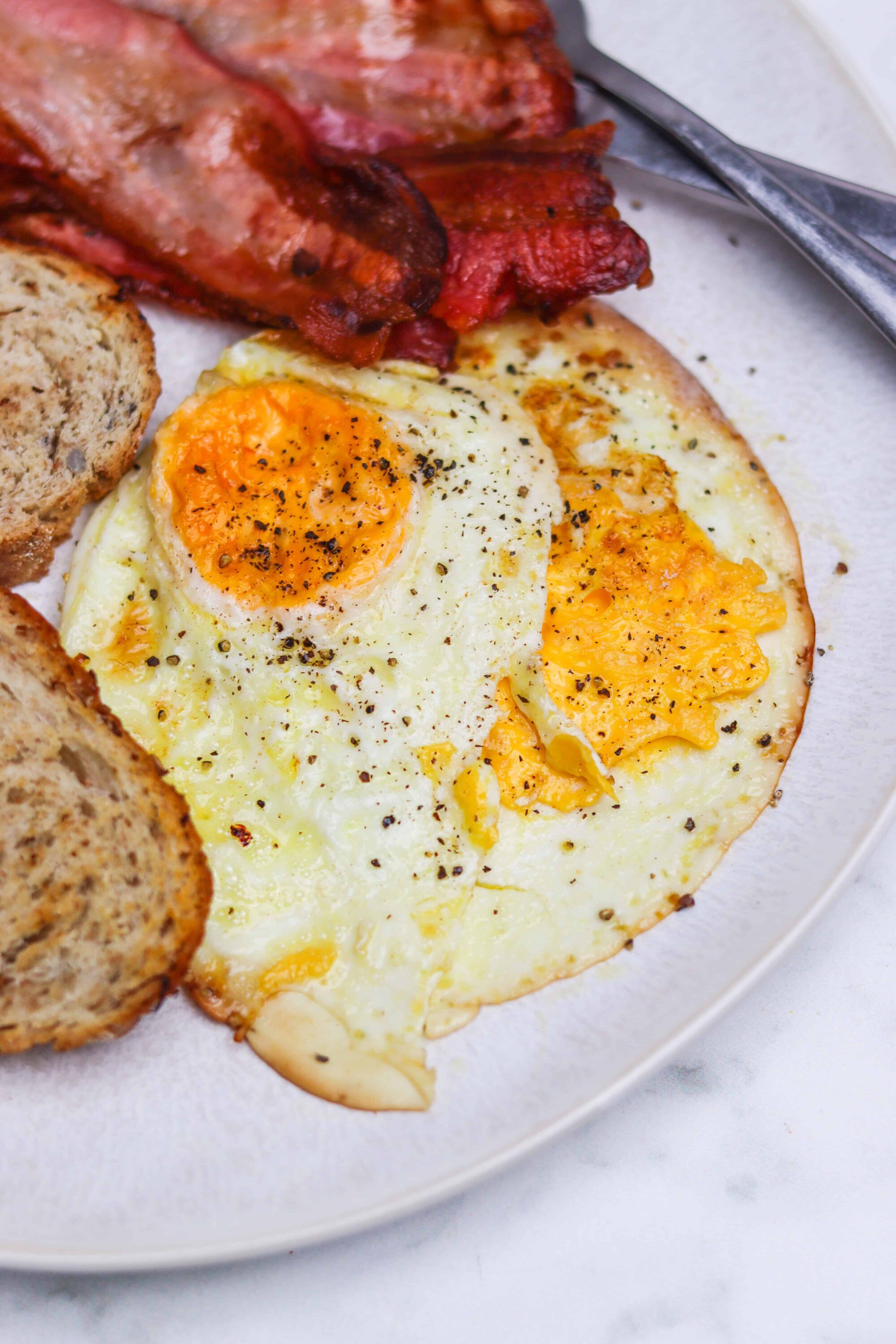 Savory breakfast with fried eggs, crispy bacon, and toasted multigrain bread, perfect for brunch or morning meals.