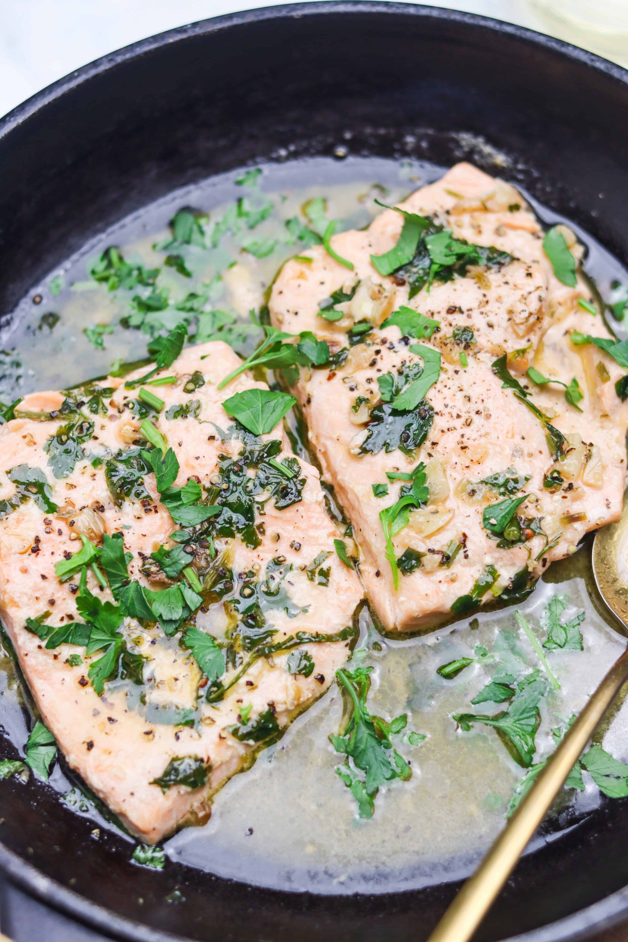 Juicy salmon fillets cooked in a skillet with fresh herbs and butter, garnished with parsley.