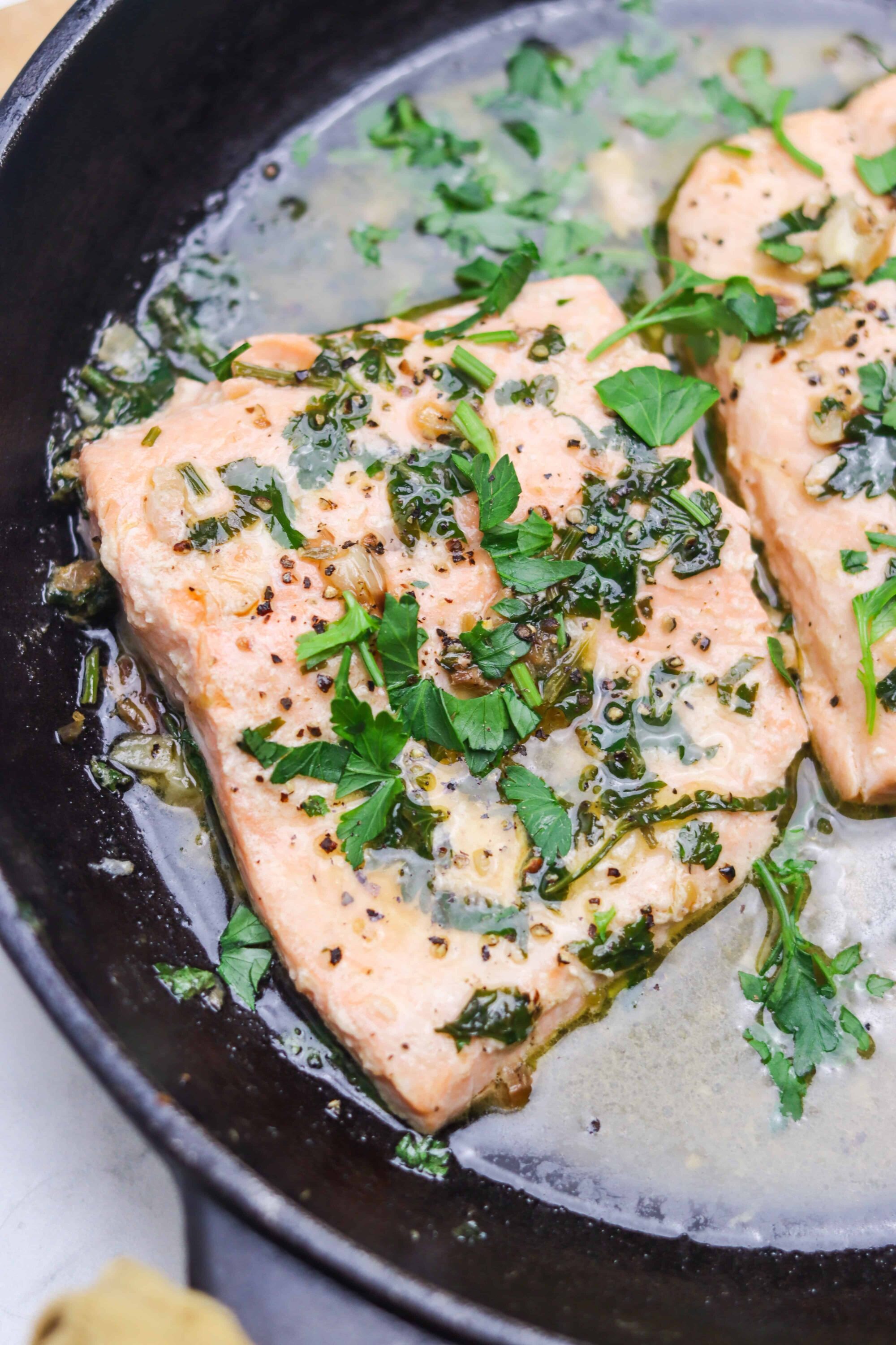 Juicy salmon fillets cooked in garlic butter with fresh herbs and black pepper, served in a cast iron skillet.
