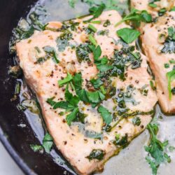 Juicy salmon fillets cooked in garlic butter with fresh herbs and black pepper, served in a cast iron skillet.