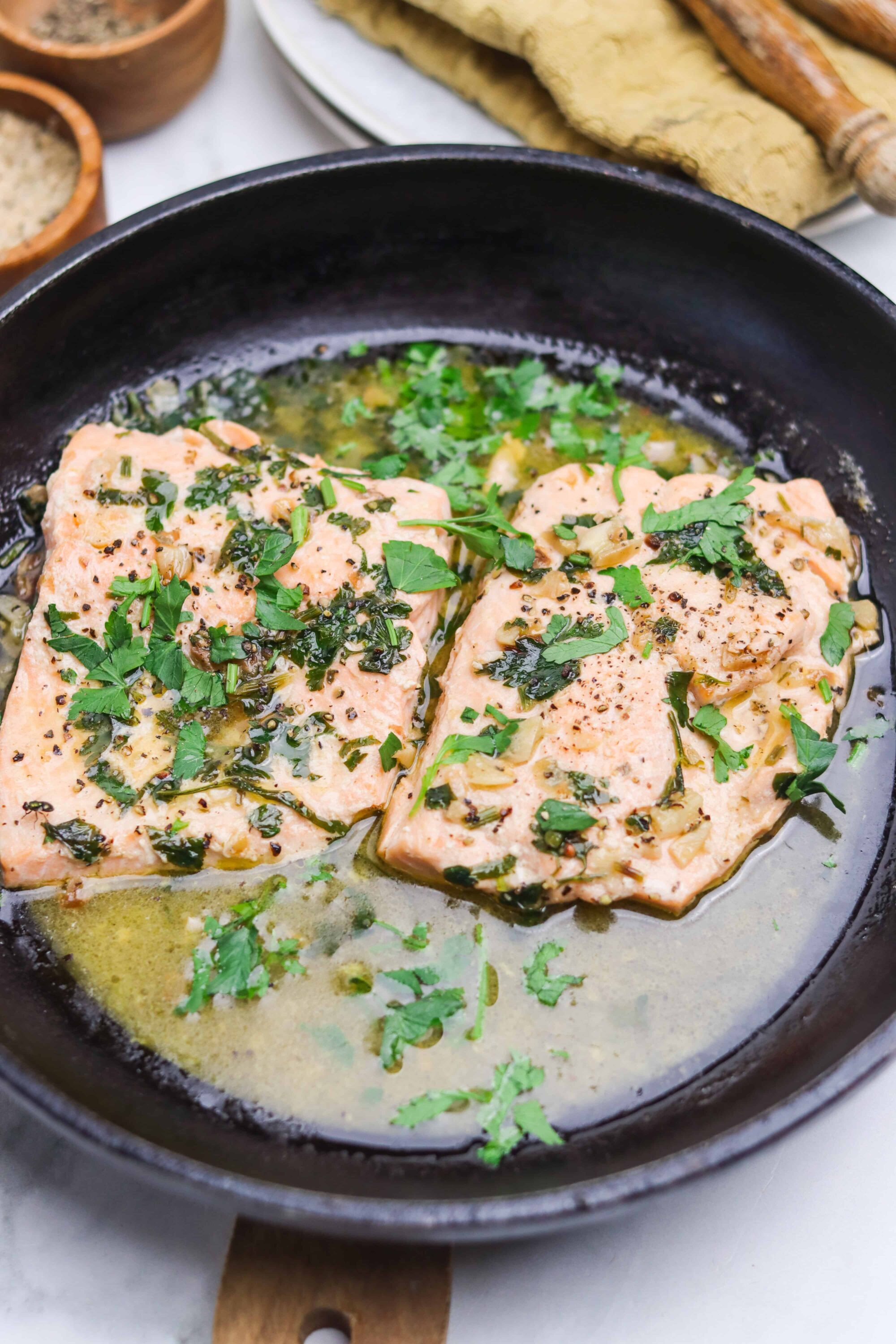 Juicy salmon fillets cooking in a skillet with garlic, herbs, and butter.