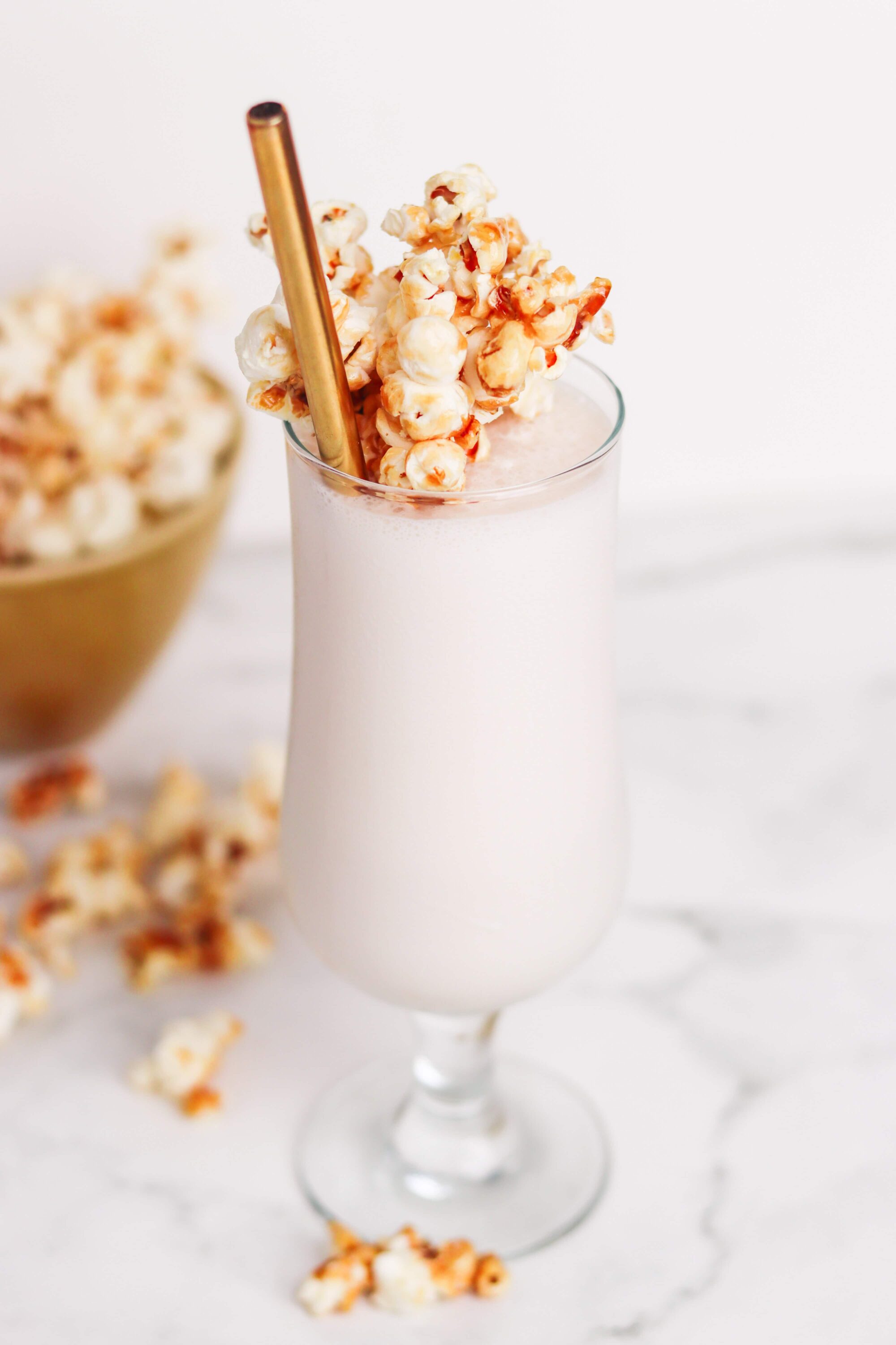 Creamy vanilla milkshake topped with caramel popcorn and a gold straw. Perfect for movie nights and snack lovers.