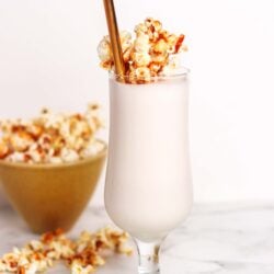 Sweet vanilla milkshake topped with caramel popcorn and a gold straw. Perfect for a delicious dessert or snack.