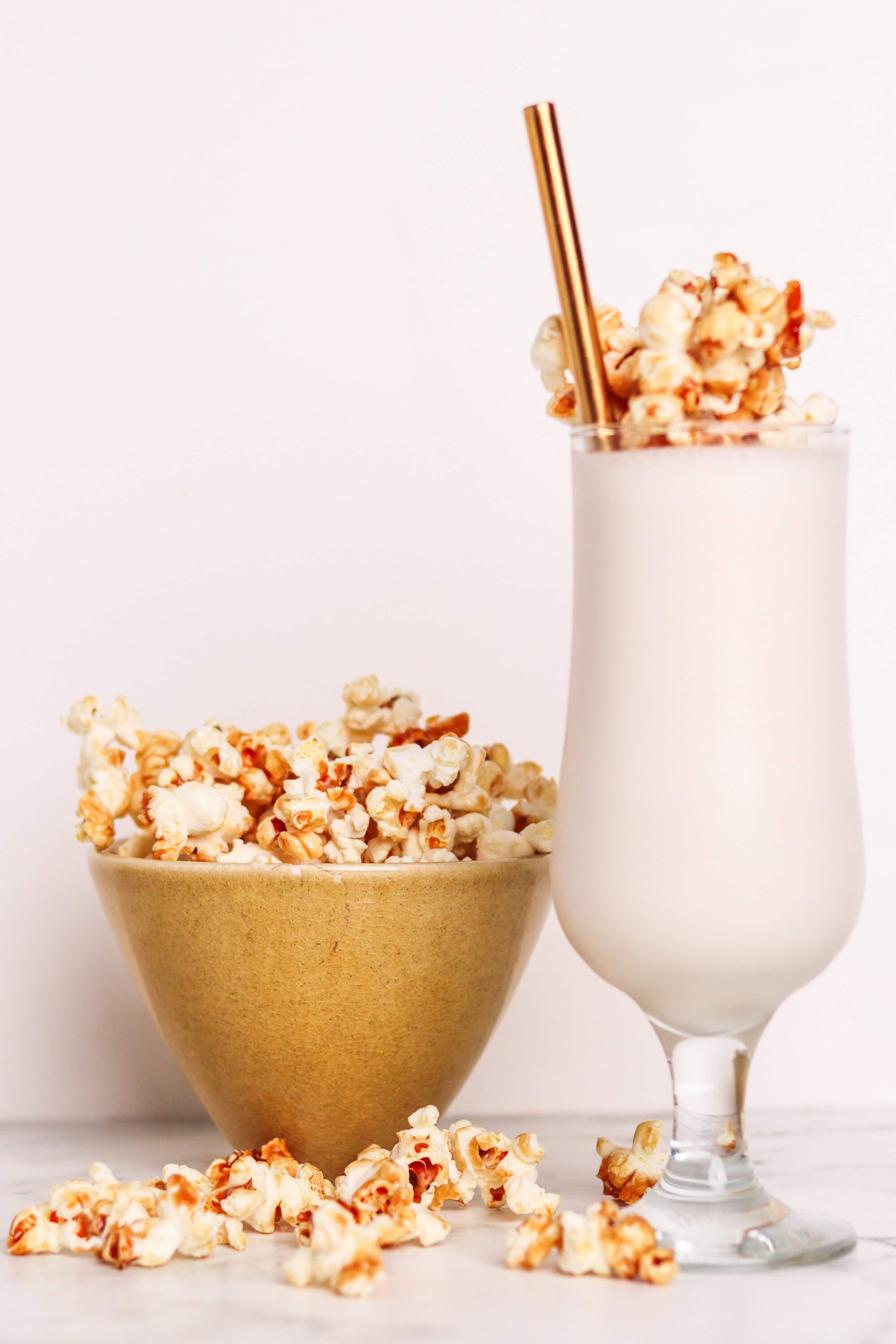 Golden popcorn in a bowl and a creamy white popcorn milkshake with a straw, perfect for movie snacks.