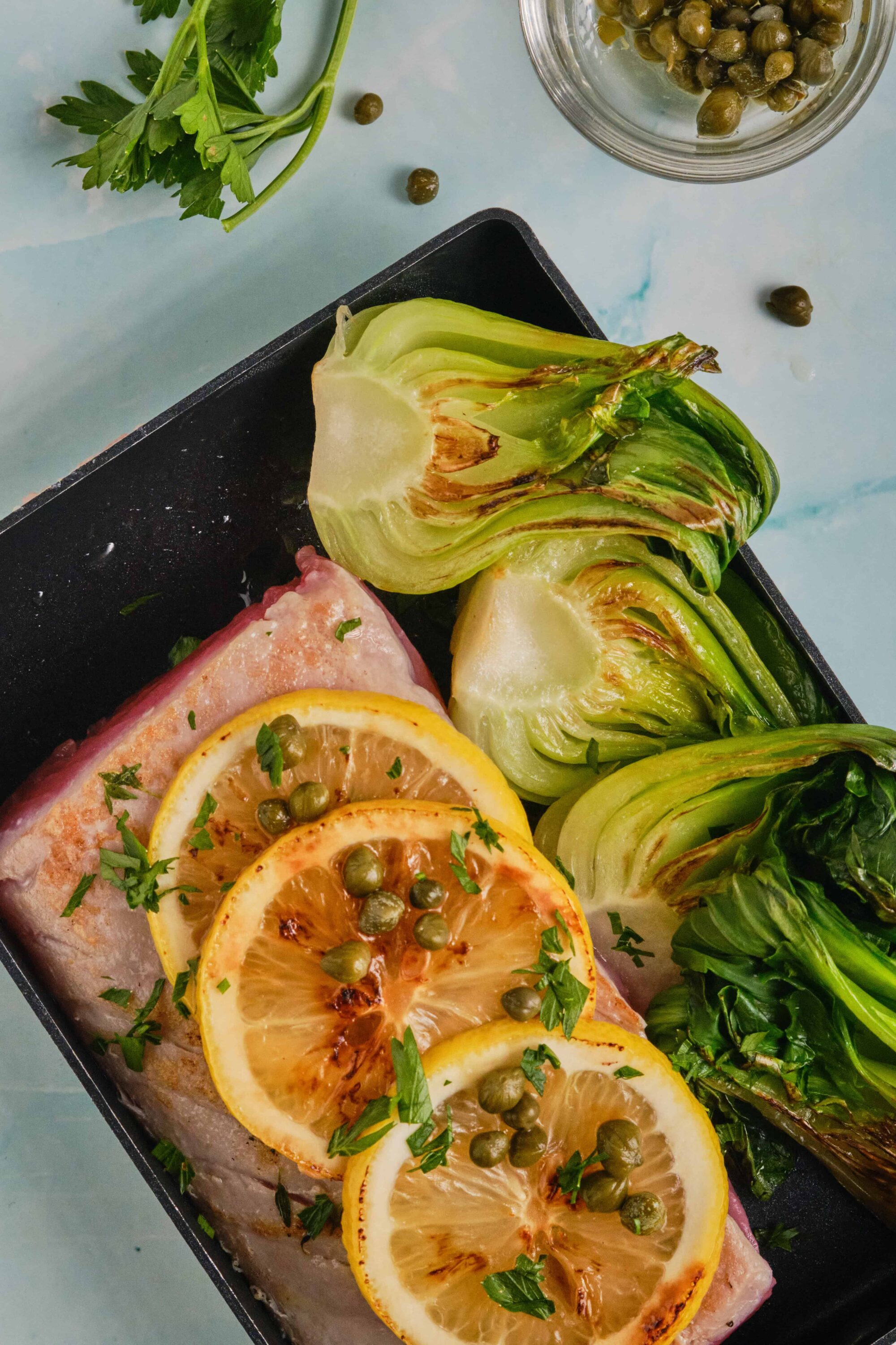 Fresh lemon slices, roasted greens, and seasoned fish in a baking dish for healthy eating.