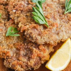 Crunchy fried breaded meat cutlets with parsley garnish and lemon wedge on a wooden plate.