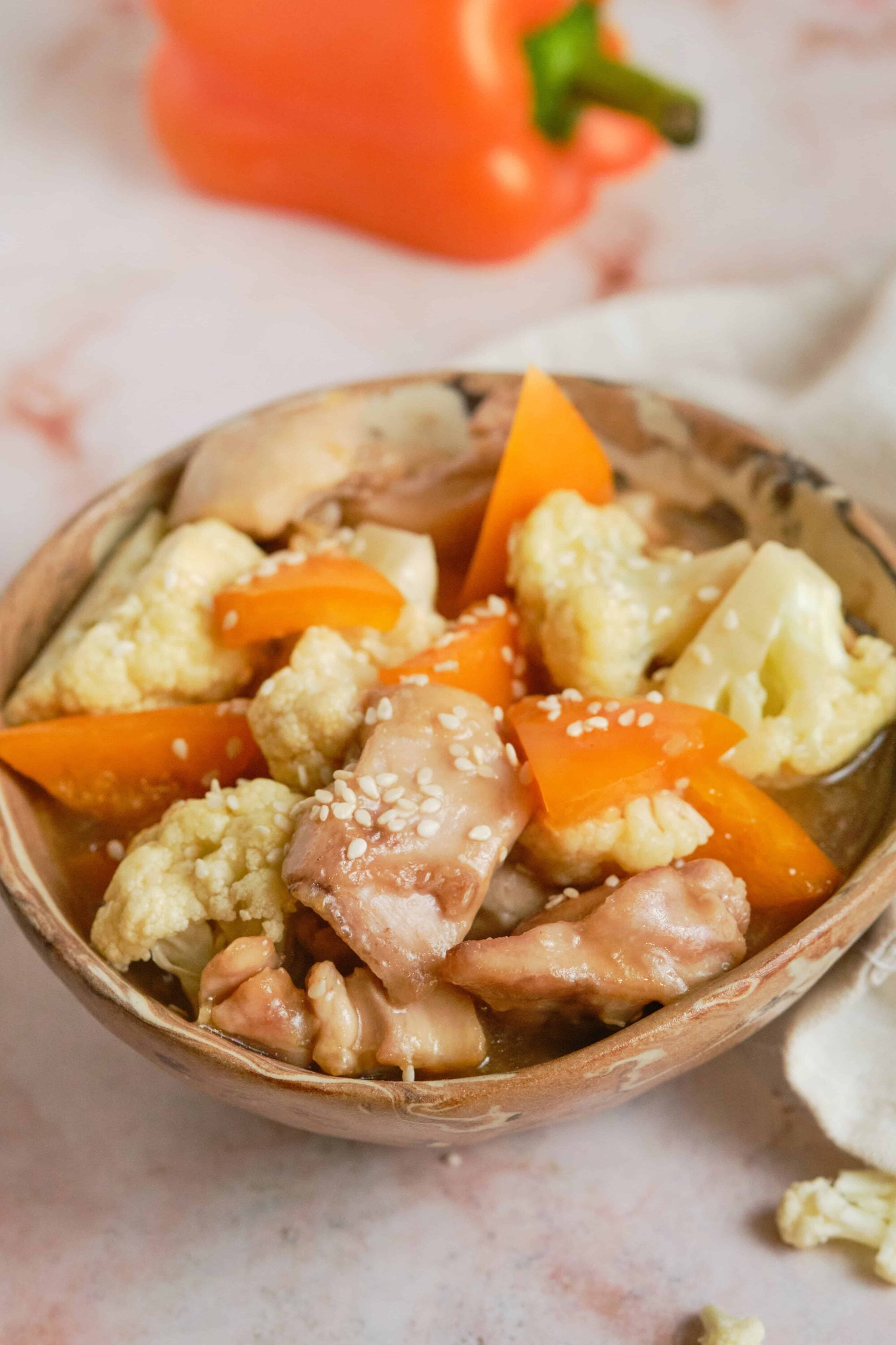 Tender cauliflower and sweet carrots in savory chicken broth with sesame seeds in a rustic bowl.
