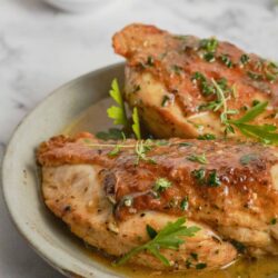 Juicy roasted chicken thighs garnished with fresh herbs on a ceramic plate.