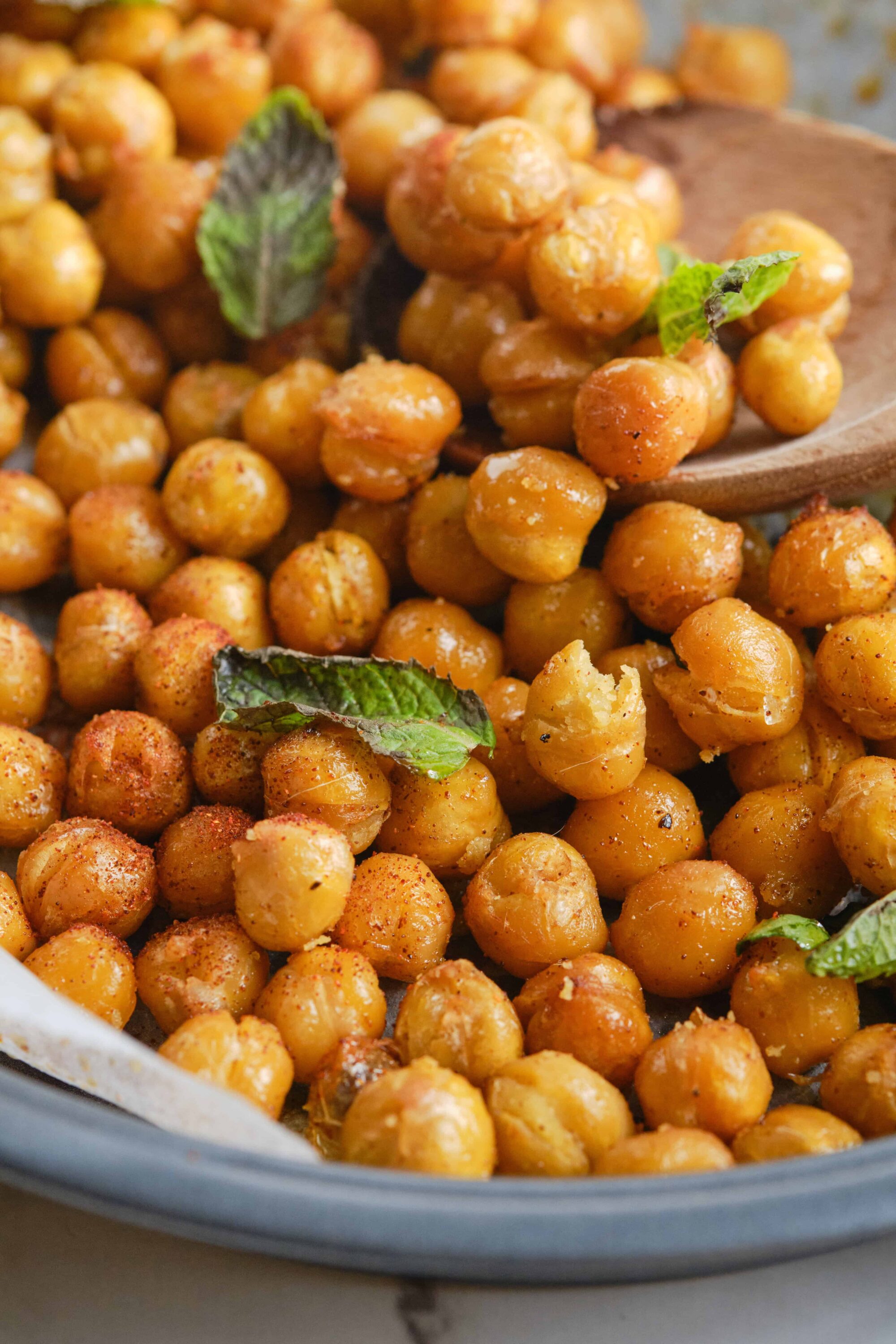 Golden roasted chickpeas with fresh mint leaves on a ceramic plate, perfect for healthy snacks or salads.