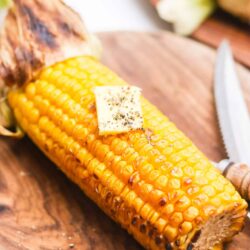 Golden grilled corn on the cob with butter and herbs on wooden serving board.
