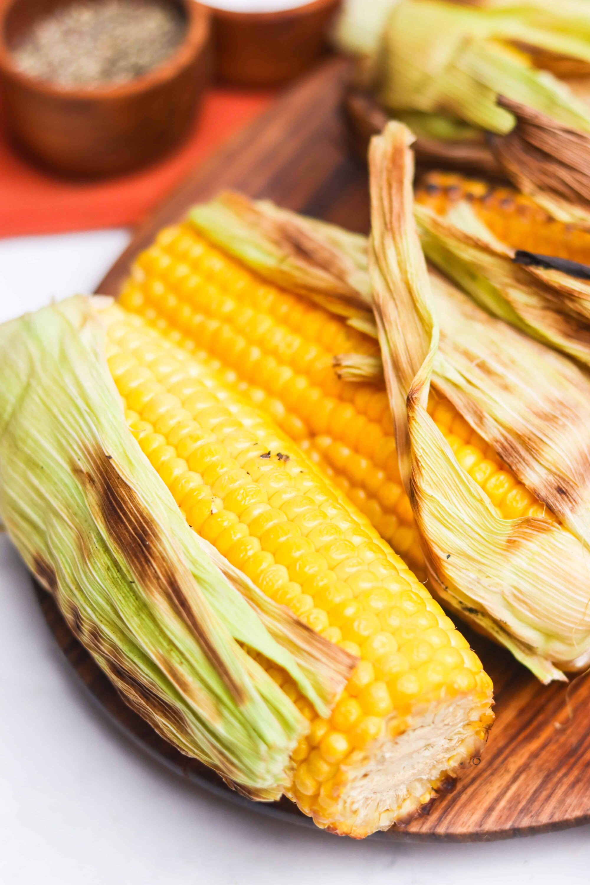Fresh grilled corn on the cob with partially peeled husk, perfect for summer recipes and outdoor cooking.