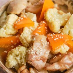 Savory vegetable and chicken stew with cauliflower, carrots, and sesame seeds in a rustic bowl.