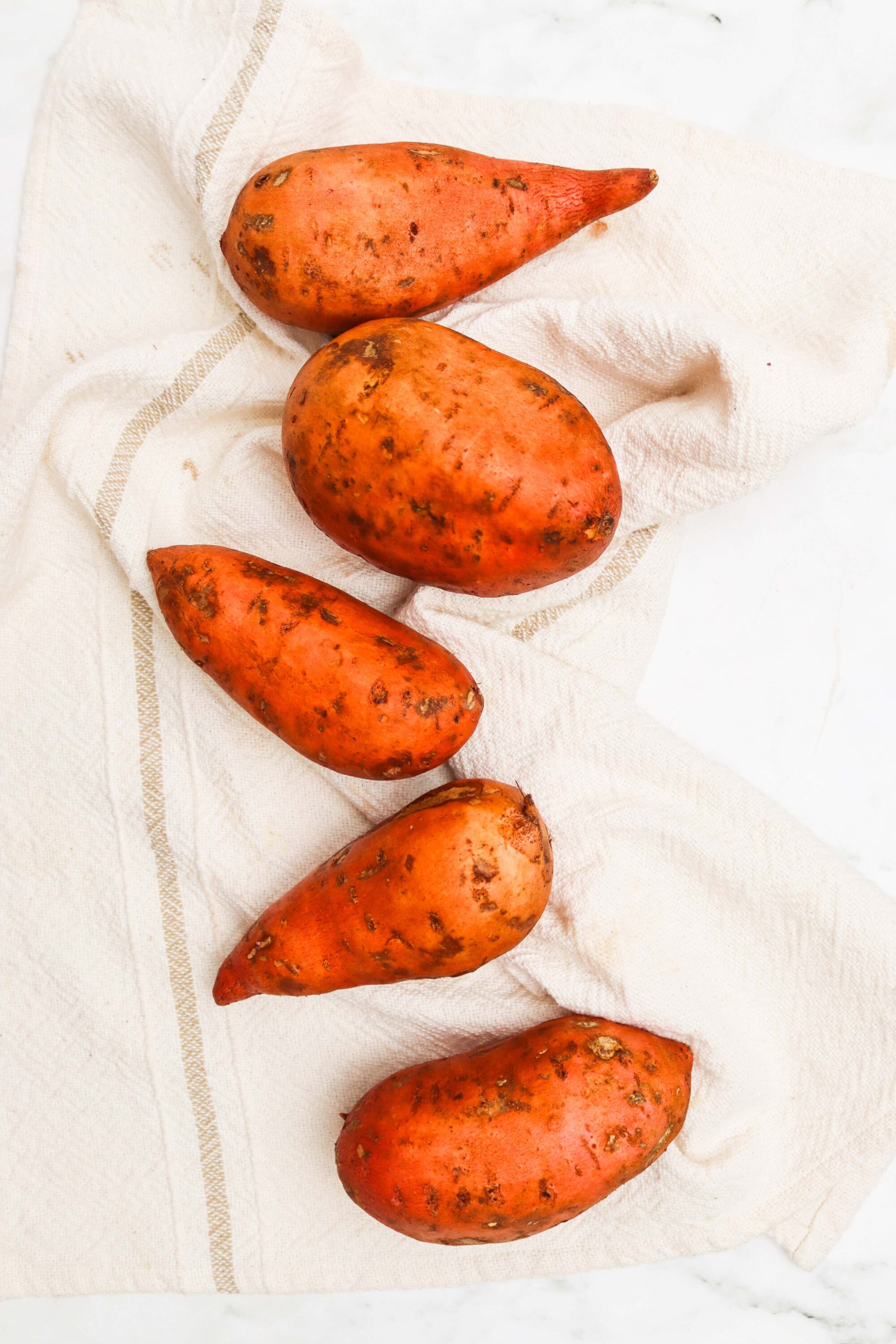 Sweet potatoes on a white cloth, fresh farm produce, healthy cooking ingredients, natural food, rustic kitchen vibe.