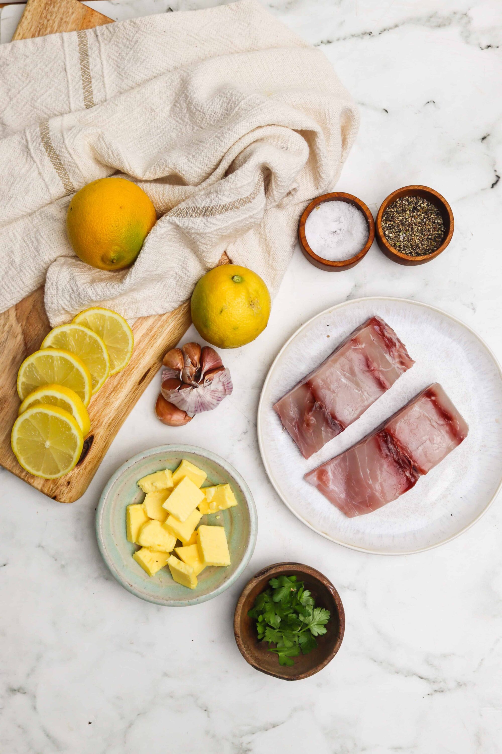 Juicy pork ribs with lemon, garlic, butter, herbs, and spices on marble surface.
