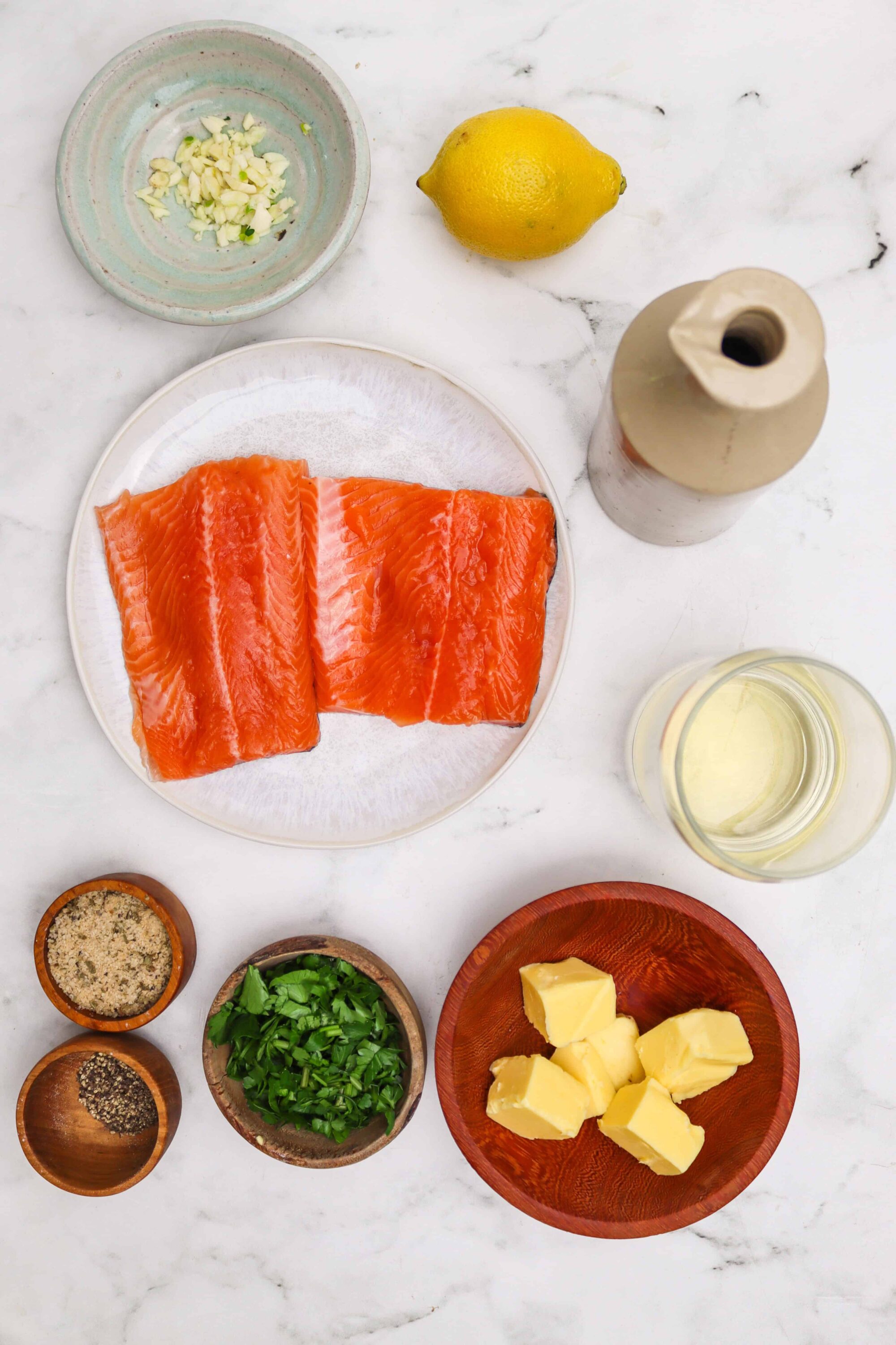 Fresh salmon fillets, garlic, lemon, butter, herbs, and seasonings for a seafood recipe.