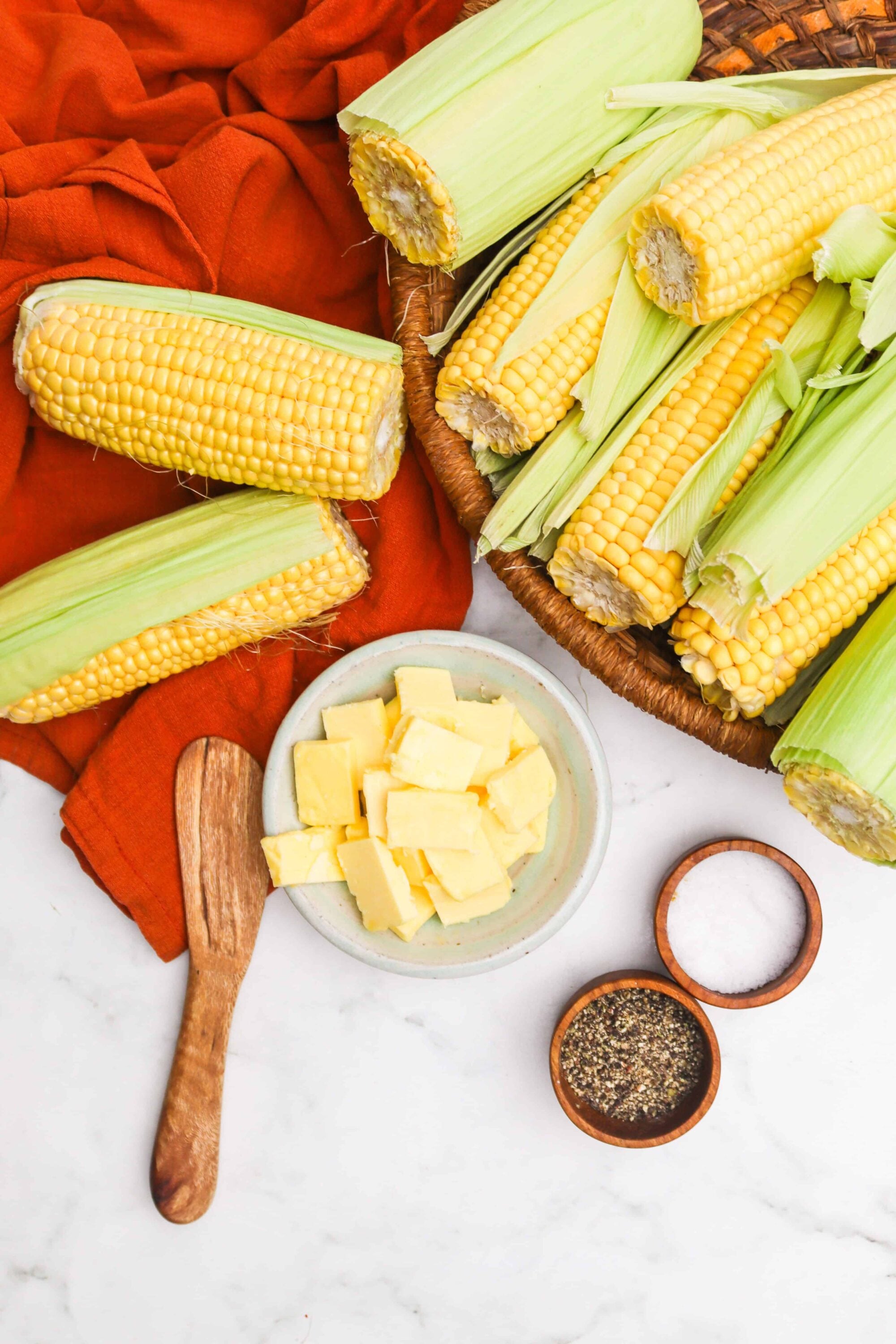 Corn on the cob with husks removed, butter, salt, and black pepper on marble surface, fresh summer corn, Baked Bree recipe ingredients.